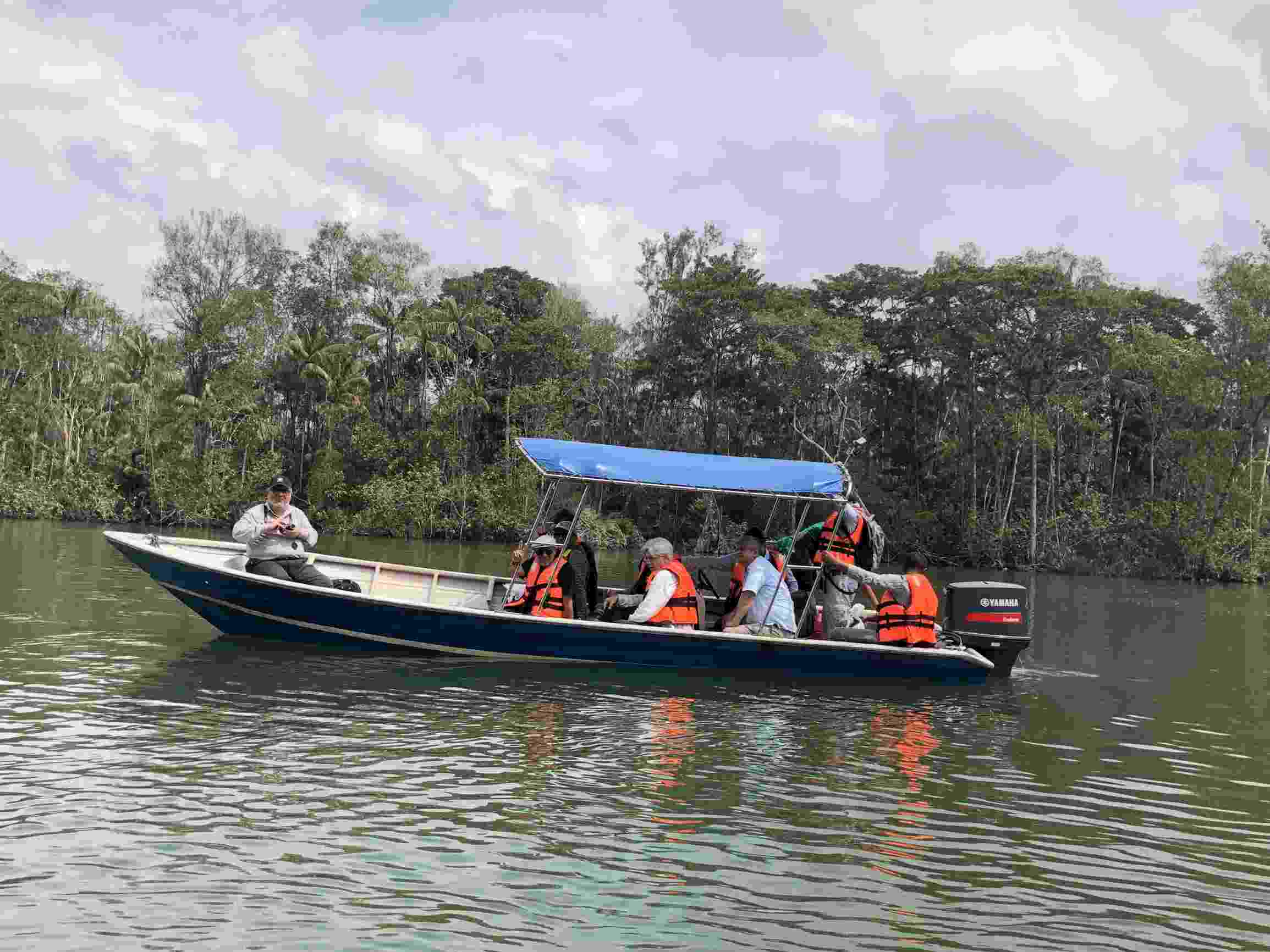 Image shows Hub members in a small motor boat on the Johor River, with green trees and palms behind